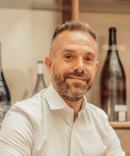 Smiling sommelier standing in a Paris wine bar with bottles and glasses.